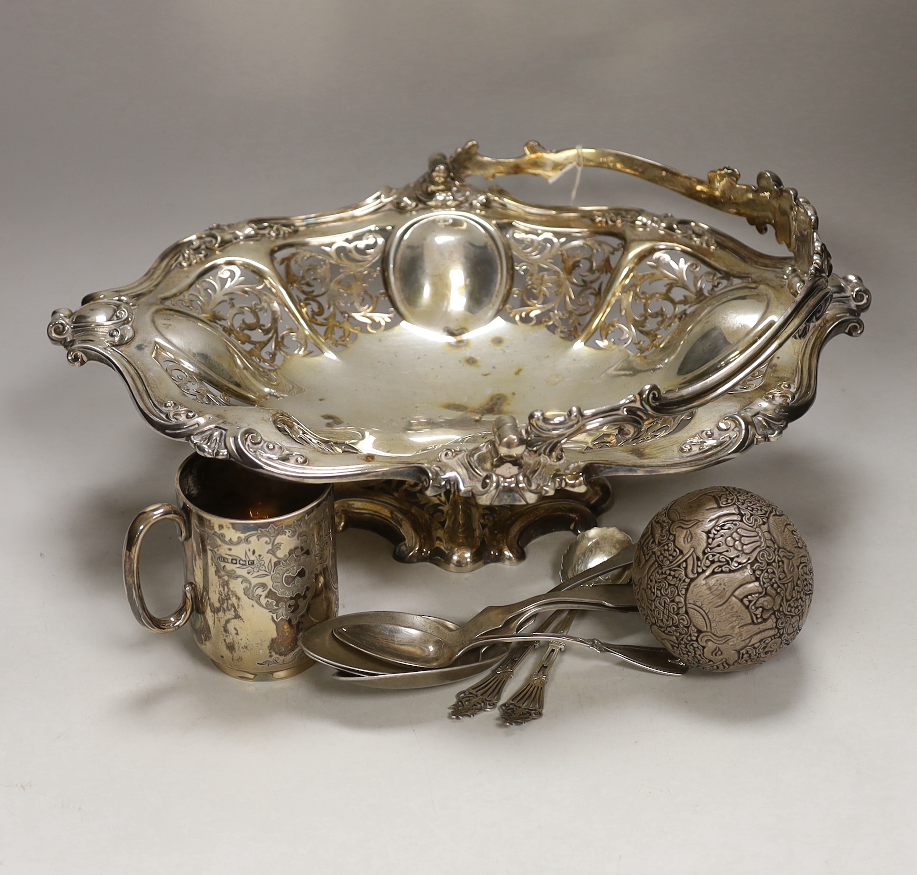 A George V silver christening mug, two silver spoons, four white metal spoons, a pierced white metal sphere? decorated with elephants and a plated bread basket.